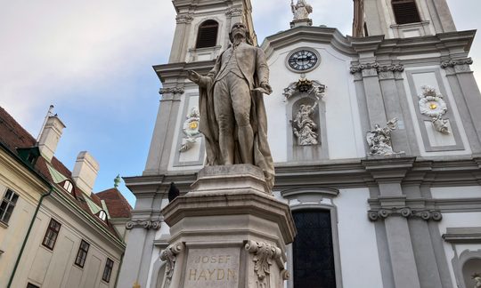 Eine Statue des Komponisten Joseph Haydn von unten, dahinter die Fassade einer Kirche.