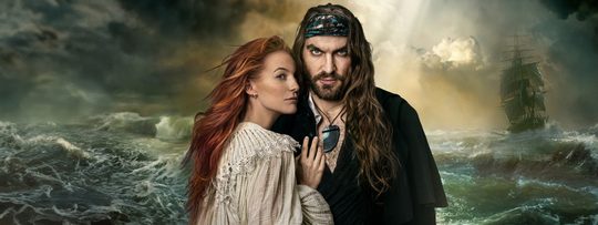 Ein Pirat und eine rothaarige Frau vor einem tosenden Meer