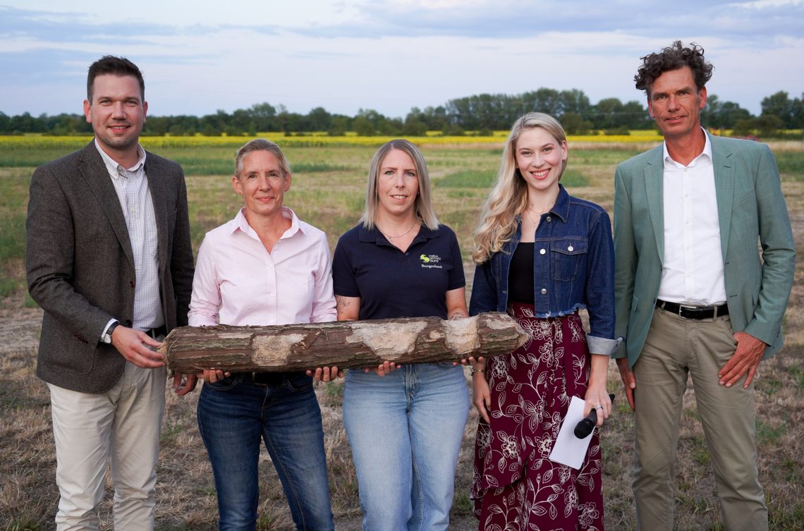 Fünf Personen halten einen Holzstamm im Burgenland vor einem Feld