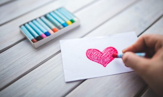 Hand mit Öl-Pastell Stift zeichnet ein Herz